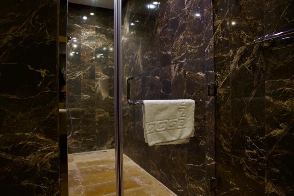 Una ducha con cerramiento de vidrio, pared de mármol y un perchero con toalla.