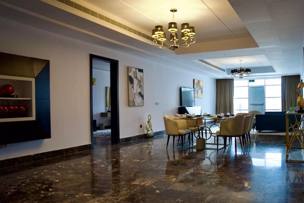 Un moderno vestíbulo de hotel con piso de mármol, una araña y un área de comedor con sillas y una mesa, además de obras de arte en las paredes.