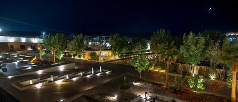 Una terraza en la azotea con mobiliario exterior, una fuente de agua y vistas del horizonte urbano nocturno.