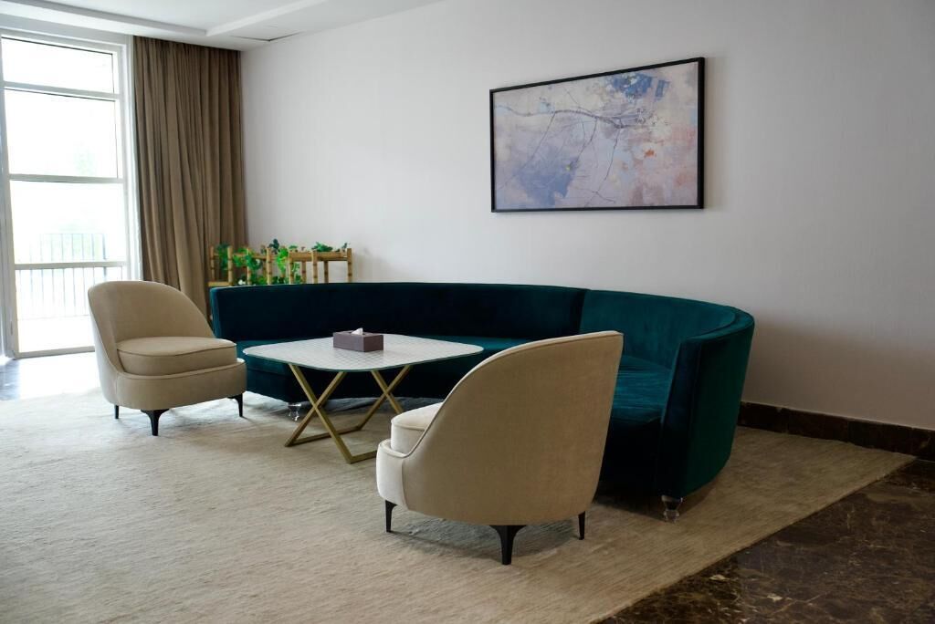 Una sala de estar con un sofá color turquesa, dos sillones, una mesita redonda y un cuadro abstracto enmarcado en la pared.