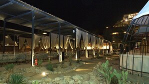 Un espace extérieur abrité, avec des chaises et des tables, un chemin et un bâtiment en arrière-plan.