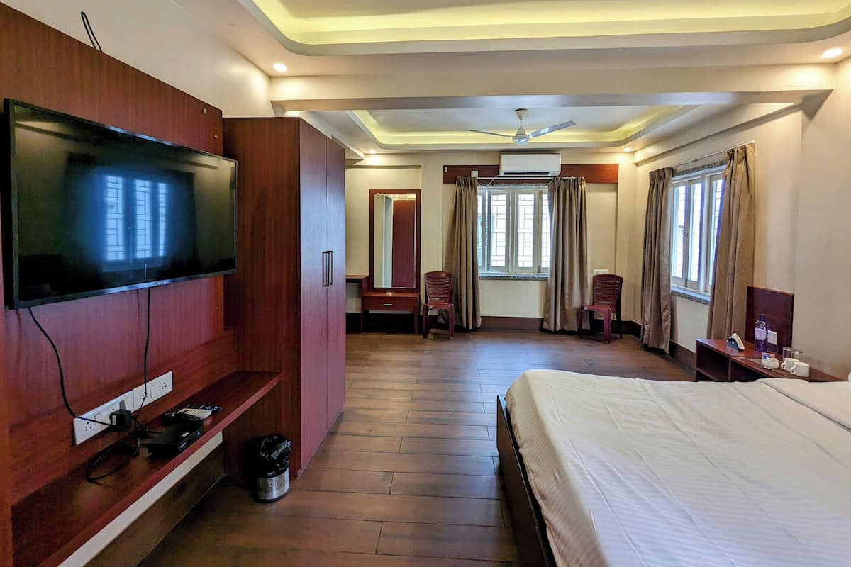 A hotel room with a bed, a TV mounted on a wooden cabinet, a ceiling fan, and a window with curtains.