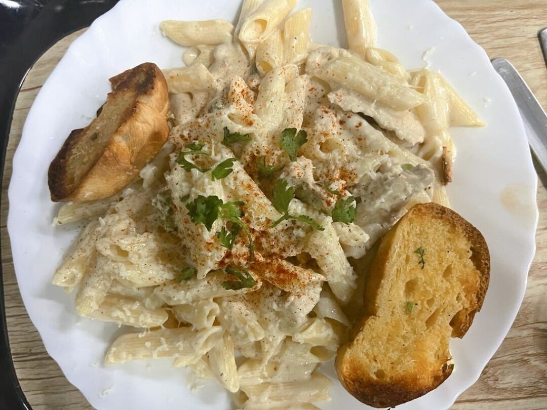 Une assiette de pâtes penne nappées d’une sauce crémeuse, garnie d’herbes fraîches, et accompagnée de tranches de pain grillé.