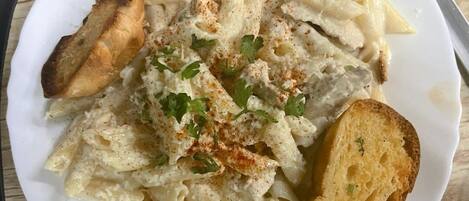 Un plato de pasta penne con salsa cremosa, adornado con hierbas, acompañado de rebanadas de pan tostado.