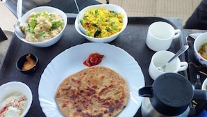 A table with a meal consisting of a flatbread, two bowls of rice dishes, a plate with a red sauce, a cup, and a thermos. - The Aster Enclave (Barasat)