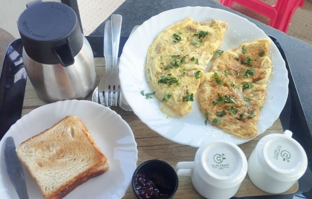 A breakfast tray with toast, scrambled eggs, and two mugs labeled "Clay Craft."