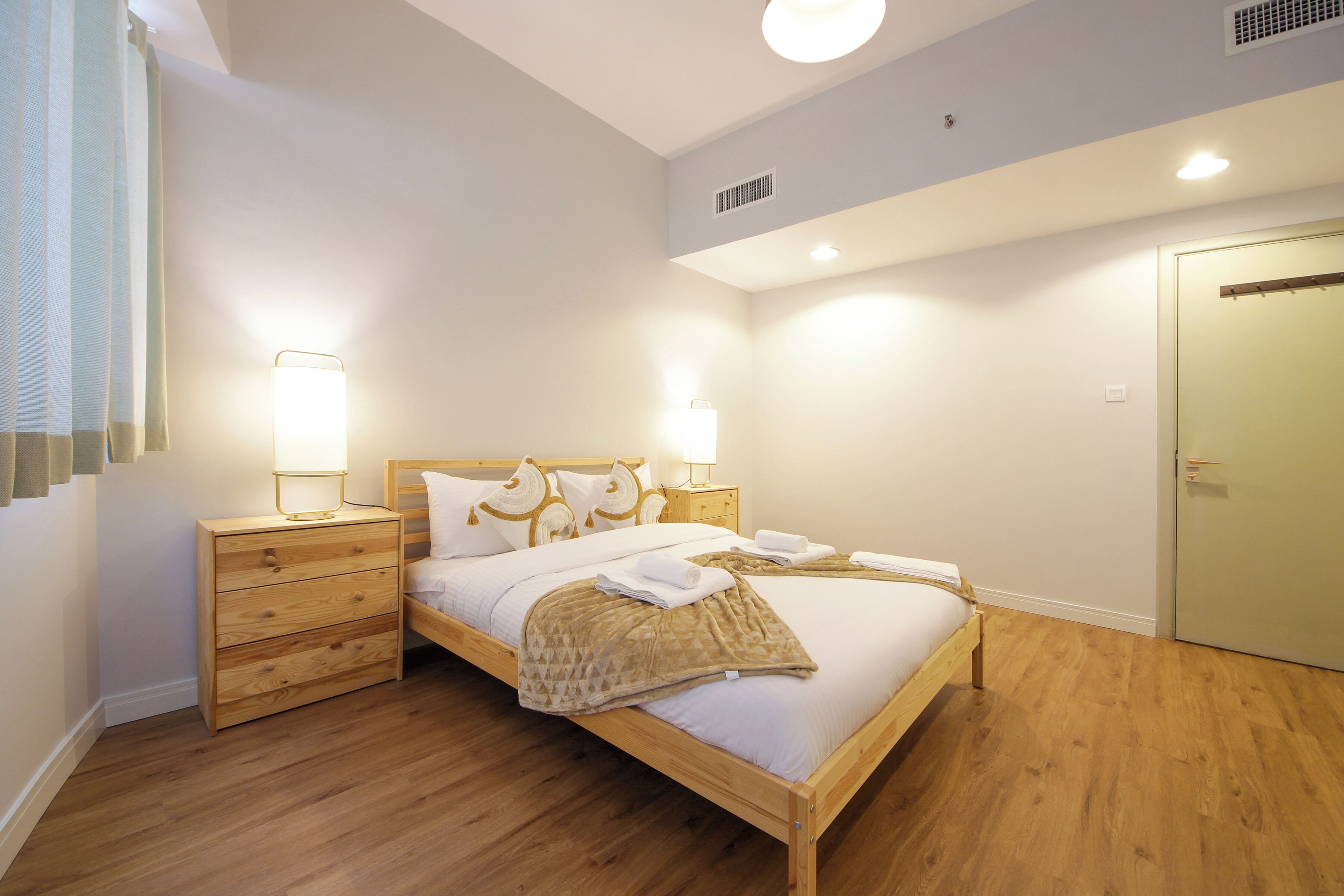 A neatly arranged bedroom with a wooden bed, bedside lamps, a nightstand, and a wardrobe.