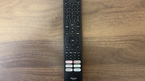 Controlo remoto preto com teclado numérico e botões de direção sobre uma superfície de madeira.