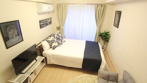 Quarto com cama, televisão em móvel, planta em vaso e janela com cortinas.