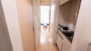 Um corredor estreito leva a um quarto com uma cama e uma janela. Uma área de cozinha é visível à direita, com uma pia e fogão.