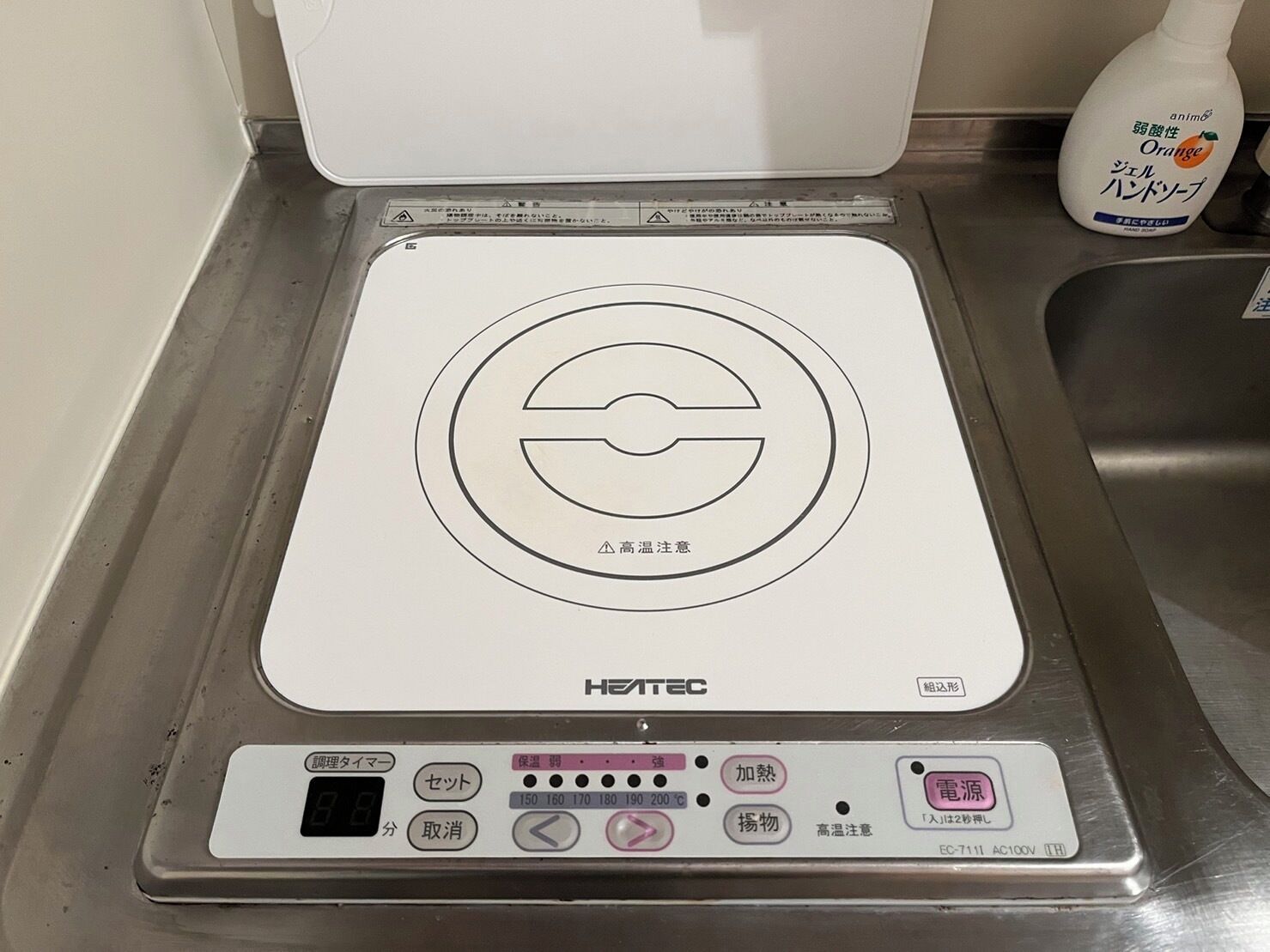 Une cuisinière électrique HEATEC dotée d’un panneau de commande numérique, d’un évier et d’un flacon de savon liquide à l’orange.
