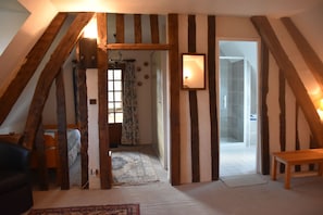 Une piĂšce avec des poutres apparentes, un lit, un banc et un miroir au mur.