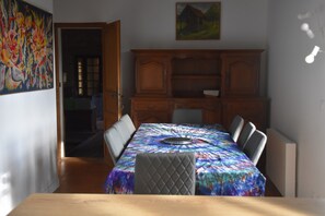 Un coin repas avec une table recouverte d’une nappe colorée, des meubles en bois et un tableau accroché au mur.