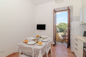 A dining area with a table set for two, a television mounted on the wall, and a kitchen area with a refrigerator.