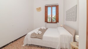 Ein Schlafzimmer mit einem Bett, einem Fenster, einem Wandbild und einem kleinen Tisch mit einer Lampe.