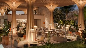 Un espace de détente extérieur doté de plusieurs types d’assises, notamment des canapés et des tables, aménagé sous une grande structure ouverte dont le plafond présente un design original.