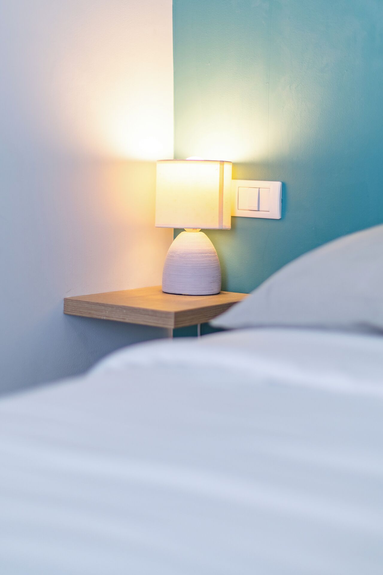 A neatly made bed with a bedside lamp on a wooden nightstand.