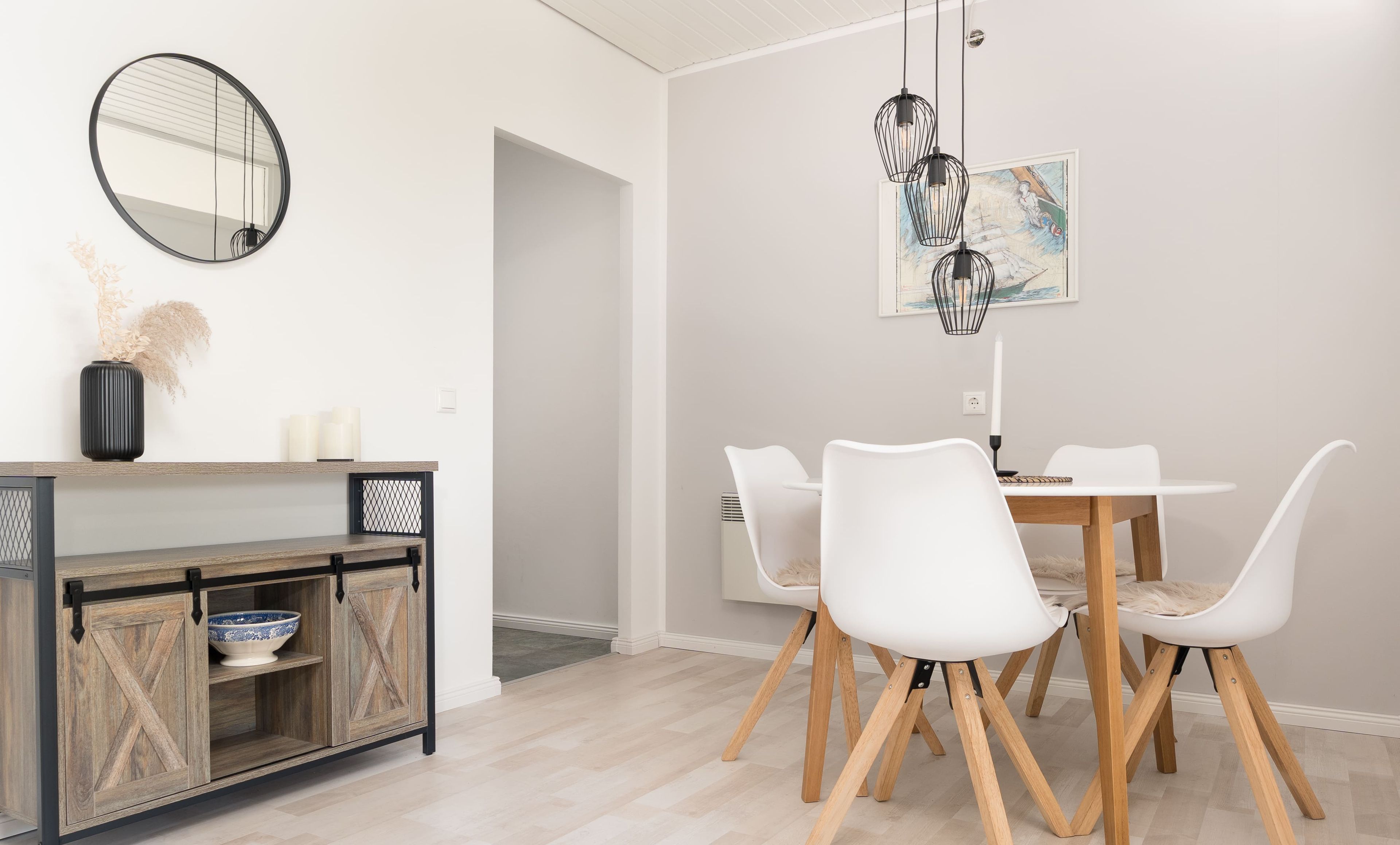 En matplats med ett vitt bord och stolar, ett träskåp med en skål, en spegel och en hängande lampa.