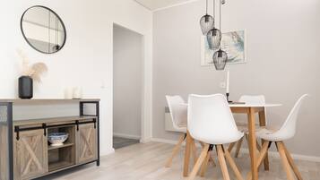 En matplats med ett vitt bord och stolar, ett träskåp med en skål, en spegel och en hängande lampa.