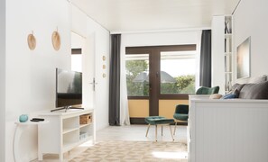 Un salon moderne doté d’un téléviseur à écran plat, de meubles blancs, d’une grande fenêtre offrant une belle vue et d’un sol à motifs.