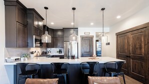 A modern kitchen with dark wood cabinets, a central island with bar stools, and pendant lighting. - Family-Friendly Escape w/ Hot Tub & Views | Near Jordanelle & Ski Resorts (Hideout)