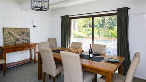 A dining area with a wooden table, beige chairs, a woven basket, wine, and a bottle. - Cartref - Cartref - Home away from Home (Mount Dandenong)