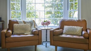 Two brown leather armchairs with white textured pillows, positioned in front of a window with a view of greenery. - Cartref - Cartref - Home away from Home (Mount Dandenong)