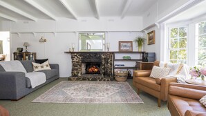 A cozy living room with a stone fireplace, a grey sofa, a brown leather sofa, and a large rug. - Cartref - Cartref - Home away from Home (Mount Dandenong)