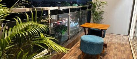 A balcony with a wooden floor, a blue cushioned stool, and a wooden table.