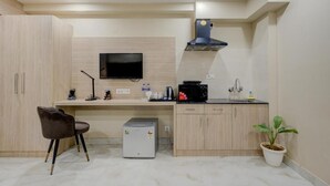 A compact kitchen with a built-in microwave, a small refrigerator, a sink, and a flat-screen TV mounted on the wall.