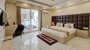 A modern hotel room with a large bed, a desk, a chair, a ceiling fan, and a view of the outdoors.
