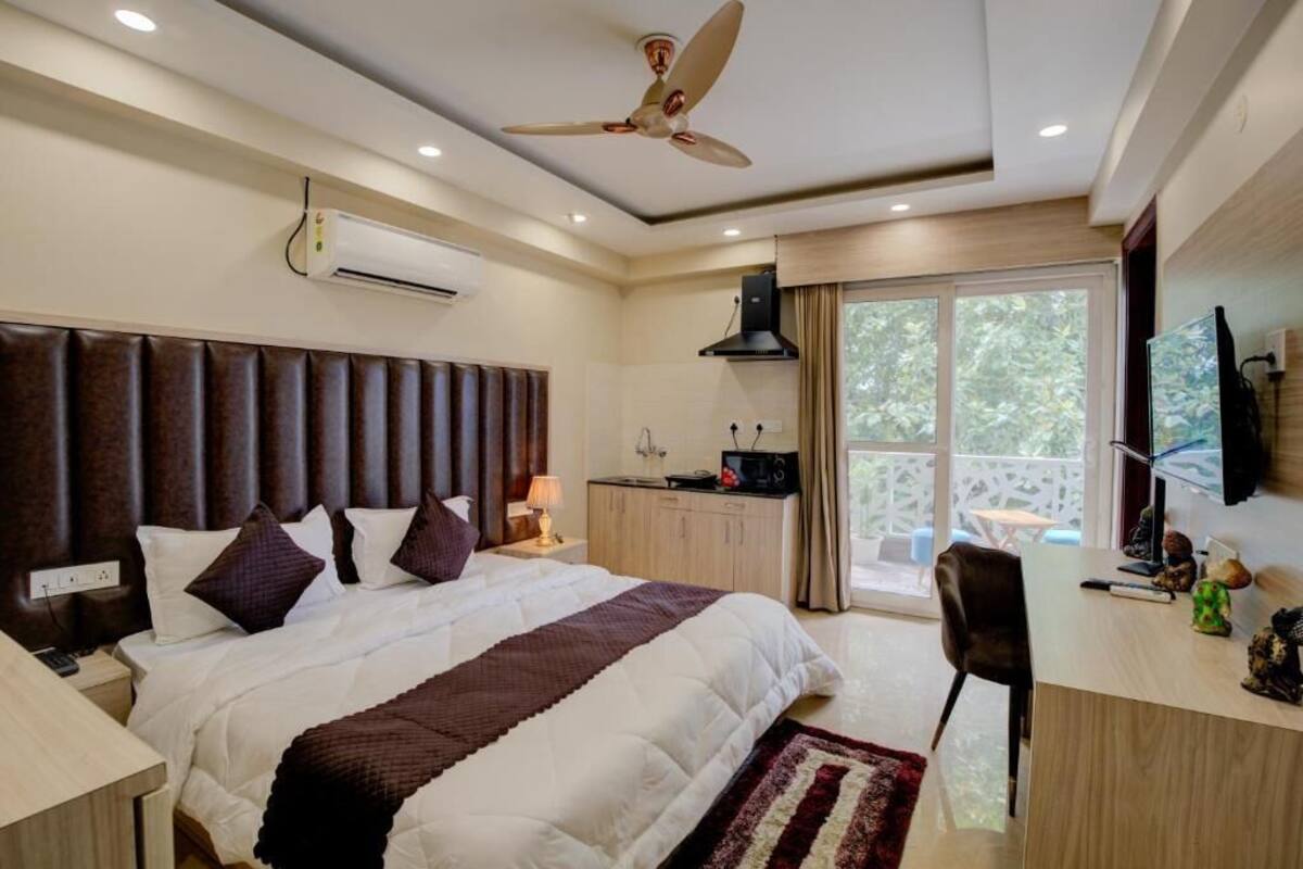 Quarto de hotel moderno com uma cama grande, escrivaninha, cadeira, ar condicionado, ventoinha de teto e vista para o exterior.