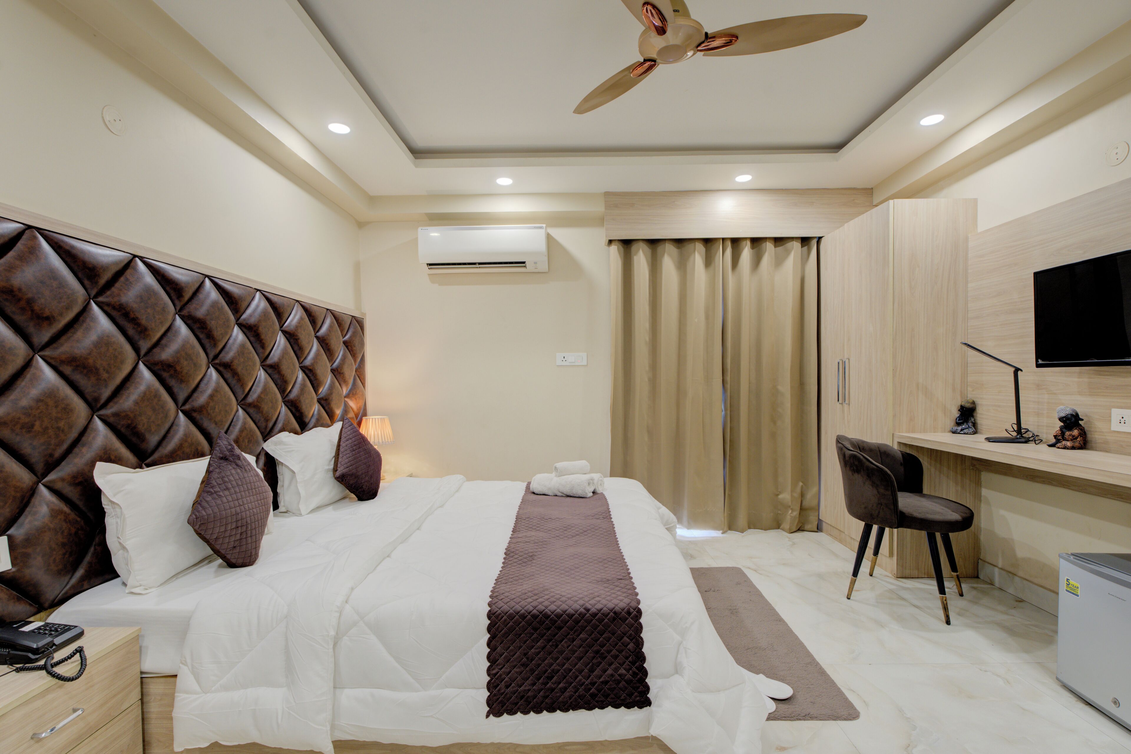 A modern hotel room with a large bed, a desk, a chair, and a ceiling fan.