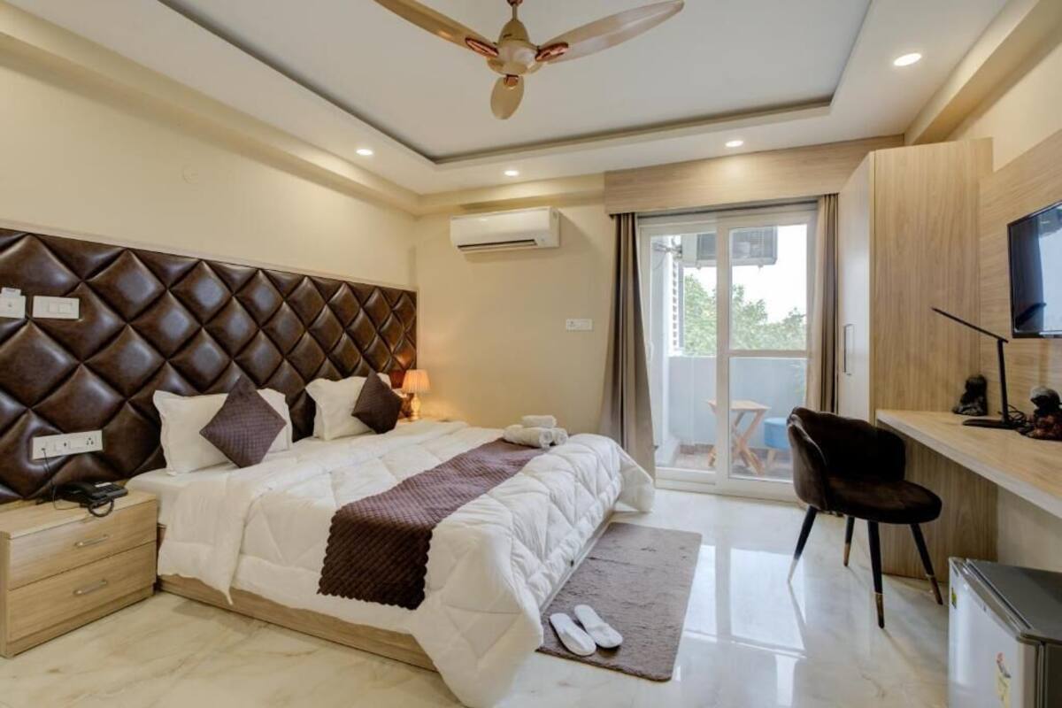 Quarto moderno com cabeceira estofada, cama com roupa de cama branca, escrivaninha com cadeira e ventoinha no teto.