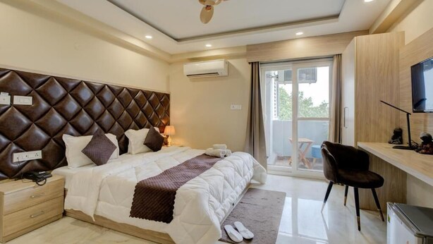 A modern bedroom with a tufted headboard, a bed with white bedding, a desk with a chair, and a ceiling fan.