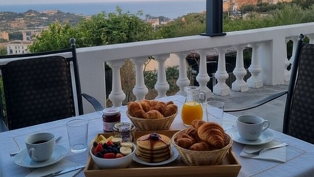 A table set with breakfast items including croissants, fruit, and pancakes, overlooking a scenic view of a coastal town. - Casa Thibaut (Poggi)