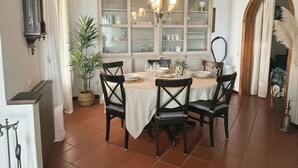 A dining area with a table set for four, surrounded by chairs, a potted plant, and a cabinet with glass doors. - Casa Thibaut (Poggi)