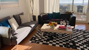 A modern living room with a grey sofa, a black sofa with colorful cushions, a checkered rug, and a large window offering a view of the city. - Casa Thibaut (Poggi)