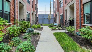 A row of brick buildings with a central walkway, surrounded by greenery and a 'For Sale' sign. - Modern Luxury | Fireplace | Rooftop Deck | Near DT (Indianapolis)