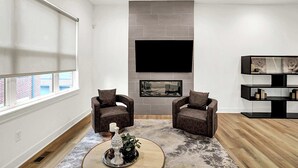 A modern living room with two leather armchairs, a fireplace, a mounted TV, and a bookshelf. - Modern Luxury | Fireplace | Rooftop Deck | Near DT (Indianapolis)