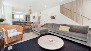 A modern living room with a grey sectional sofa, a wicker chair, a round coffee table, and a staircase with wooden railings. - Modern Luxe Retreat | Hot Tub | Garage | Near DT (Indianapolis)