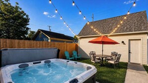 A backyard with a hot tub, outdoor seating, and string lights. - Modern Luxe Retreat | Hot Tub | Garage | Near DT (Indianapolis)