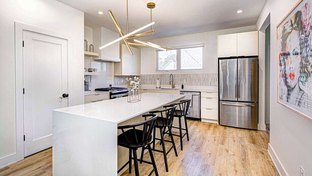 A modern kitchen with a central island, stainless steel appliances, and a contemporary light fixture. - Stylish 4BR | Hot Tub | Patio | Firepit | Near DT (Indianapolis)