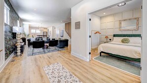 A modern hotel room with a large bed, a seating area with a sofa and chairs, a dining table, and a staircase leading to another level. - Stylish 4BR | Hot Tub | Patio | Firepit | Near DT (Indianapolis)