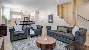 A modern living room with two grey sofas, a round coffee table, and a staircase with wooden railings. - Stylish 4BR | Hot Tub | Patio | Firepit | Near DT (Indianapolis)