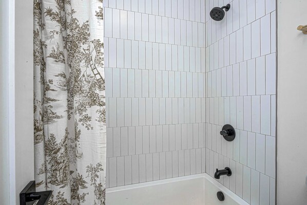 Ein Badezimmer mit weißen Fliesenwänden, einer Dusche mit schwarzem Wasserhahn und einem Vorhang mit floralem Muster.