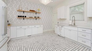 A modern kitchen with white cabinets, black and white patterned flooring, and a chandelier.