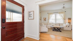 A living room with a wooden door, a white wall, and a beige sofa.