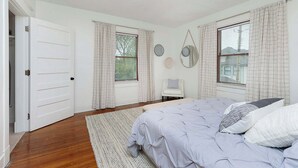 A bedroom with a bed, a chair, a door, and windows with curtains.