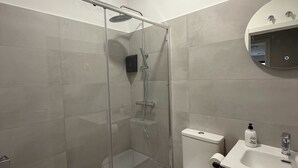 A modern bathroom with a glass-enclosed shower, a toilet, a sink with a mirror, and wooden cabinetry. - Hostal Alcorcon (Alcorcón)
